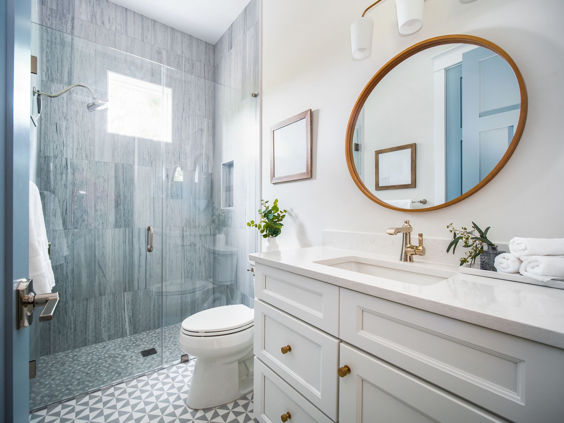 A bright bathroom with a white vanity, a large round mirror, and a tiled shower with glass doors.