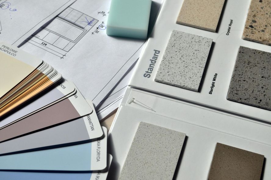 Color swatches, countertop samples, and blueprints arranged on a surface, showcasing design options for a project.