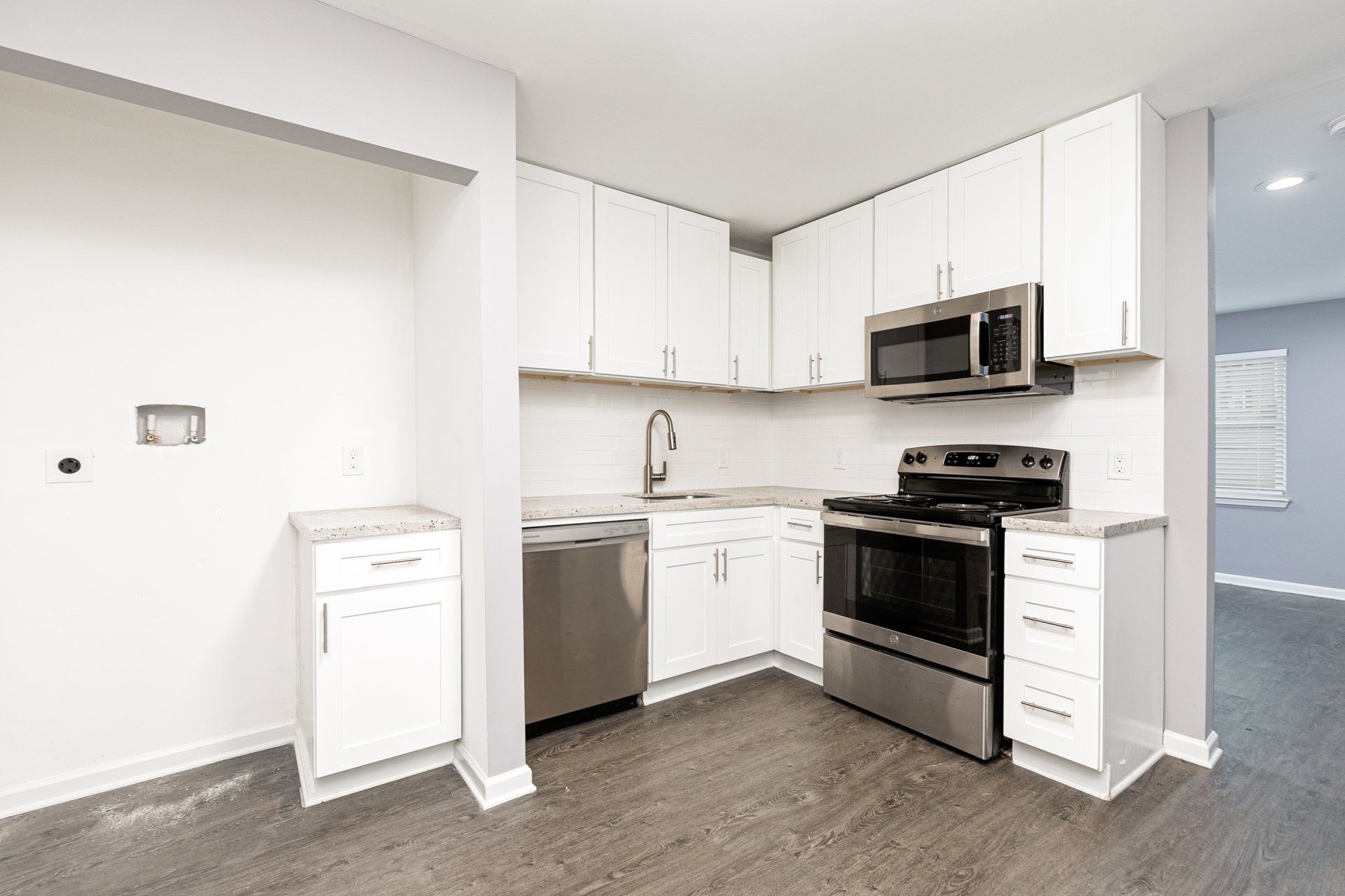 Apartments Near Hartsfield-Jackson International Airport - Gardens at Park West - Kitchen With Stainless Steel Appliances, New White Kitchen Cabinets, Granite Countertops, Tile Backsplash, And Vinyl Plank Flooring.