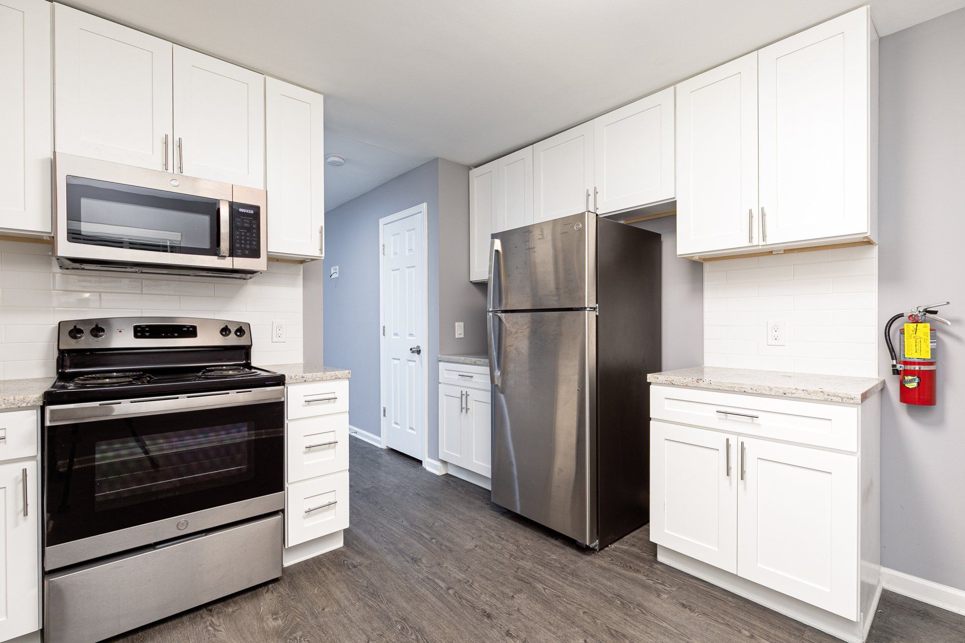 Apartments Near Hartsfield-Jackson International Airport - Gardens at Park West - Kitchen With Stainless Steel Appliances, New White Kitchen Cabinets, Granite Countertops, Tile Backsplash, And Vinyl Plank Flooring.