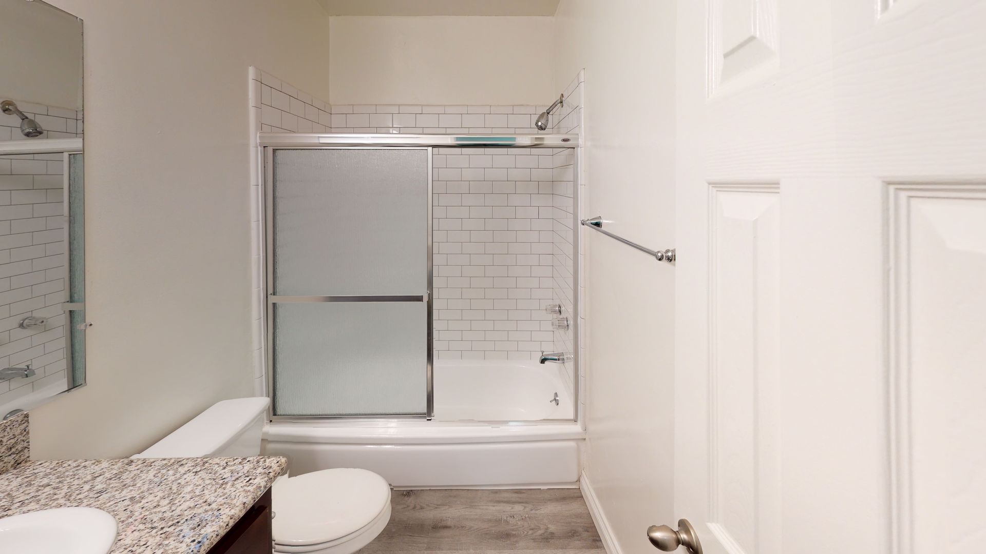 Bathroom with white walls, tub/shower, toilet, and vanity with granite countertop.