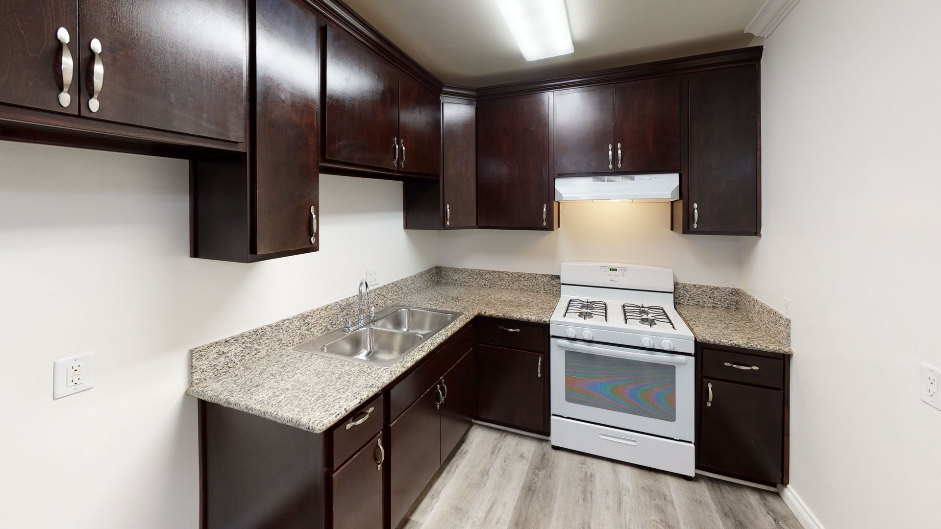 Dark wood kitchen cabinets with speckled countertops, a white oven, and a stainless steel sink.