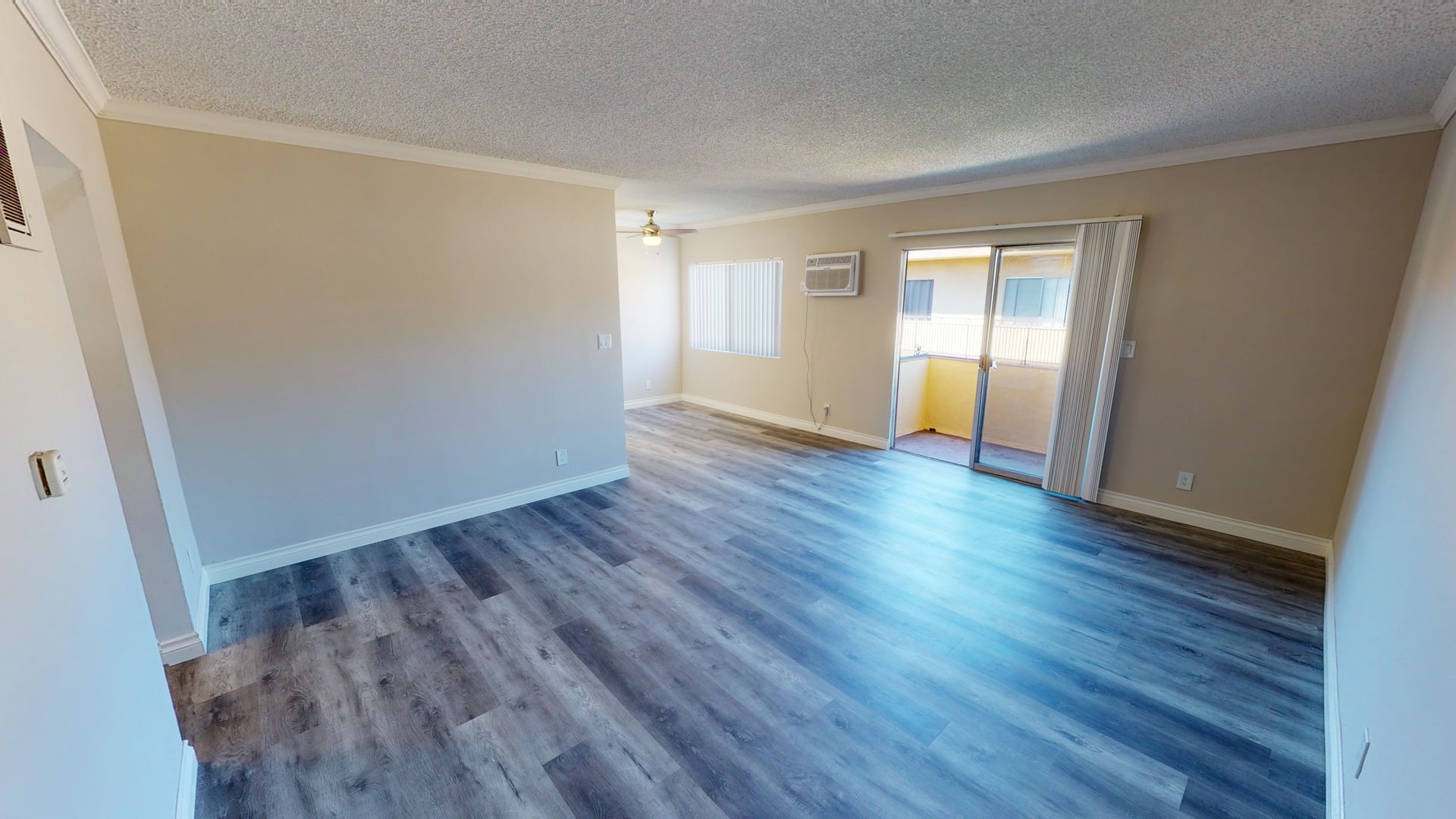 Empty living room with wood-look flooring, beige walls, sliding door to balcony, and a window.