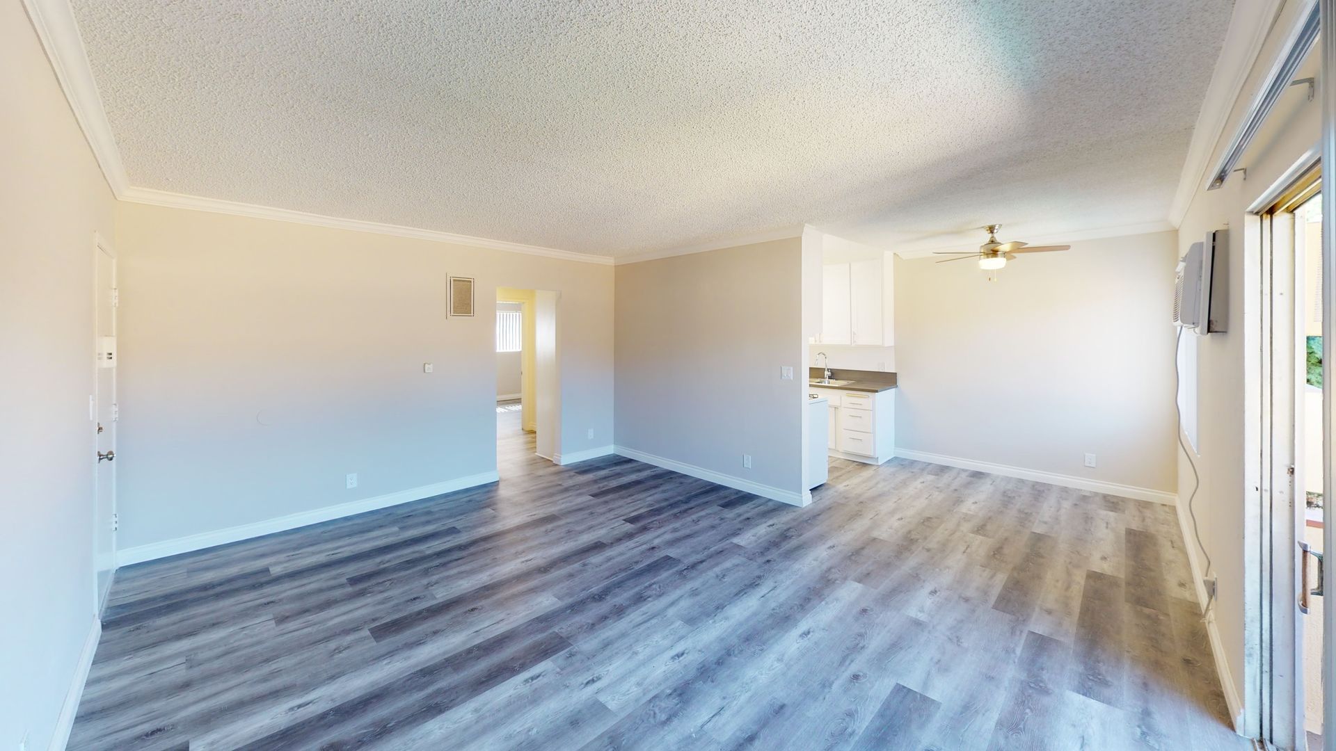 Empty living room with gray wood-look floor, white walls and ceiling, and a sliding glass door.