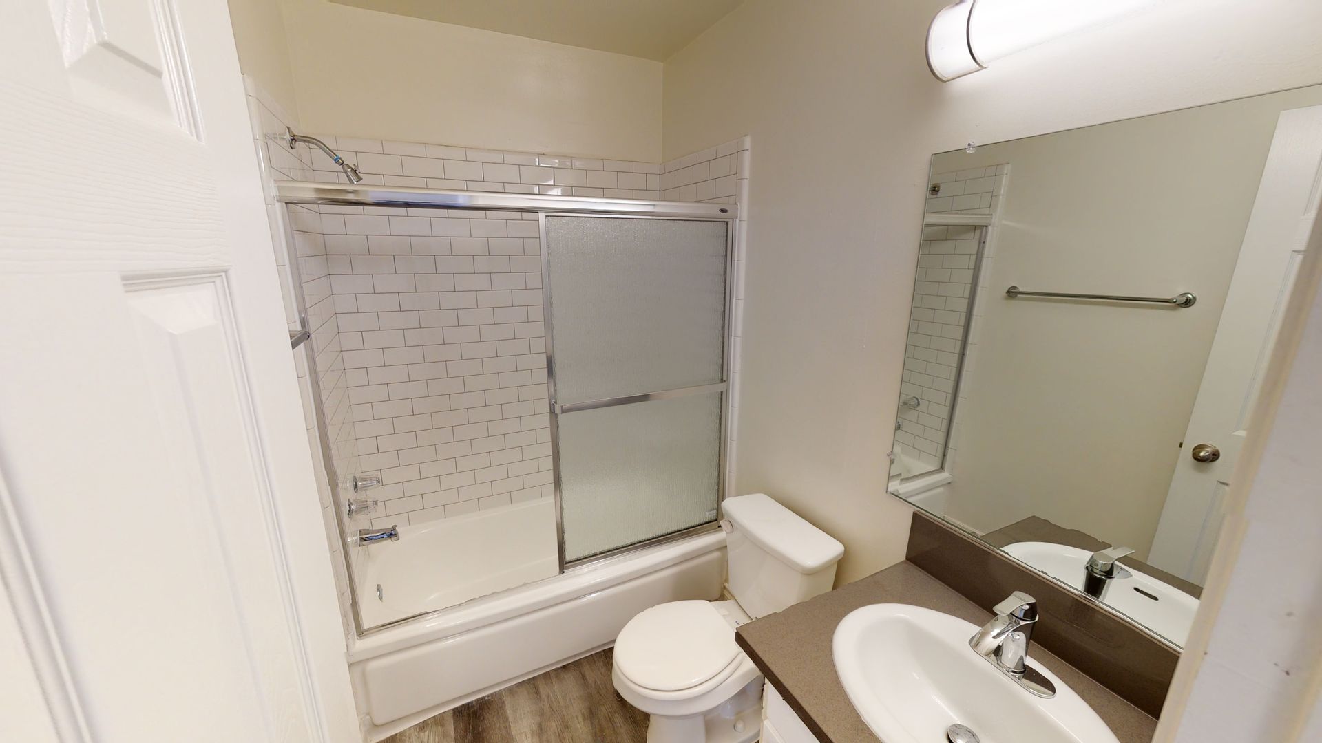 Bathroom with white walls, shower/tub combo, toilet, and sink with mirror.