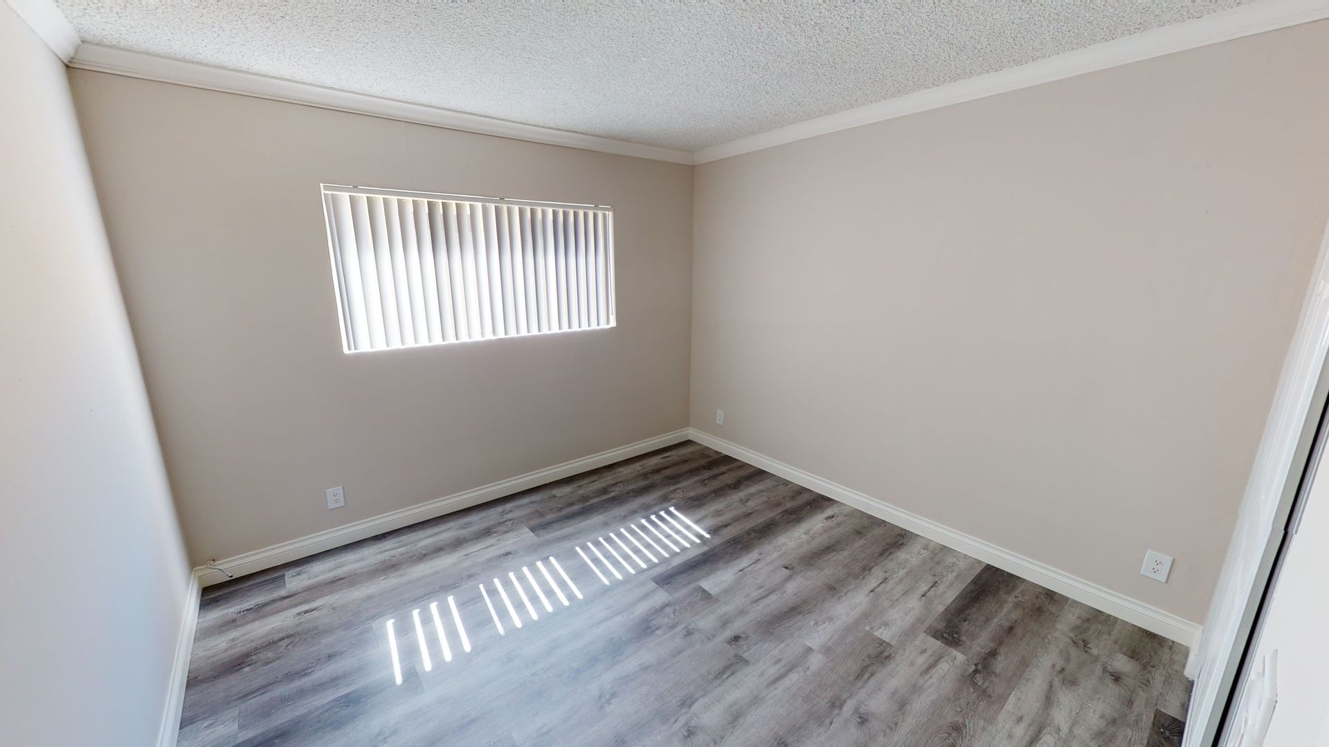 Empty room with light gray walls, window with blinds, and wood-look flooring.