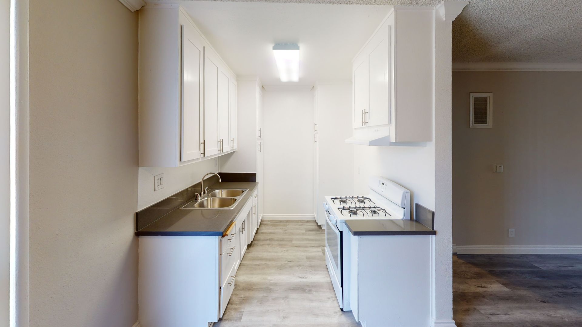 Narrow kitchen with white cabinets, countertops, and appliances. Gray floors.