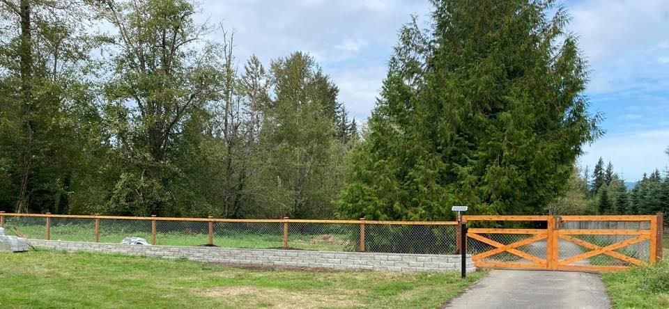 A wooden fence surrounds a grassy field with trees in the background.