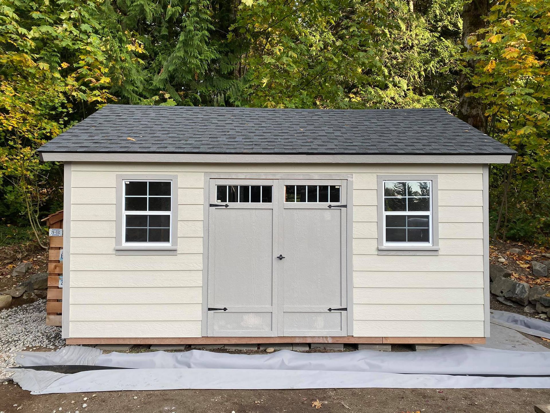 A white shed with a black roof and two windows