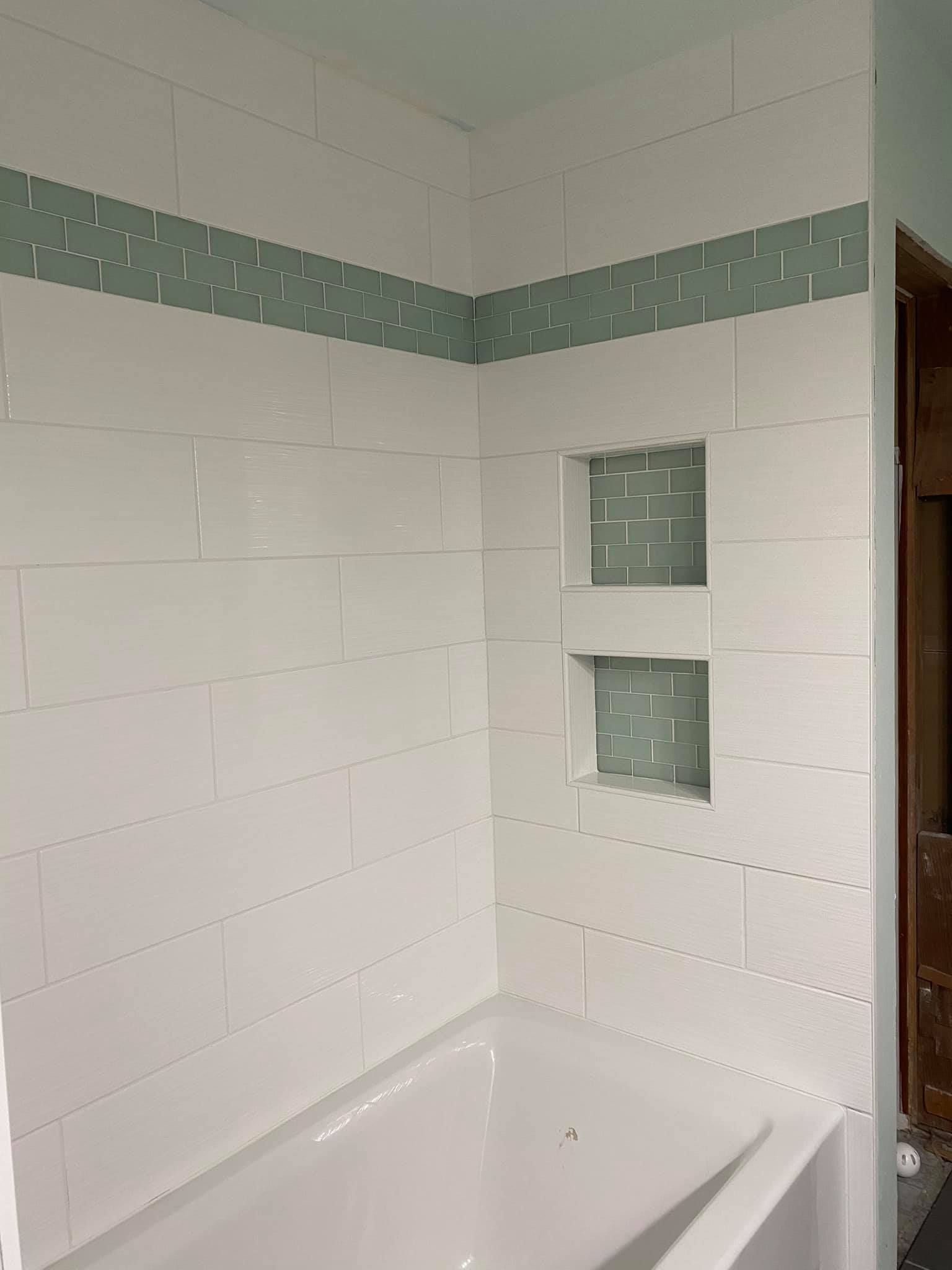 A bathtub in a bathroom with white tiles and green trim.