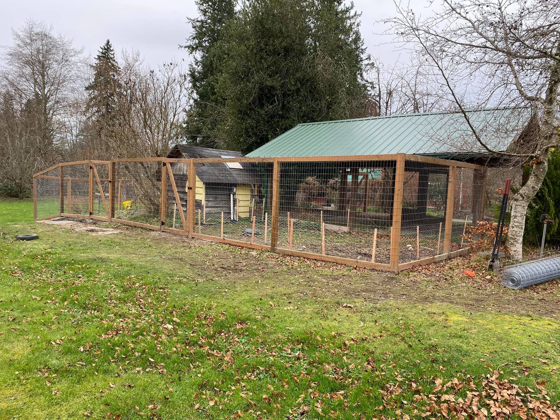 A wooden fence is surrounding a chicken coop in a yard.