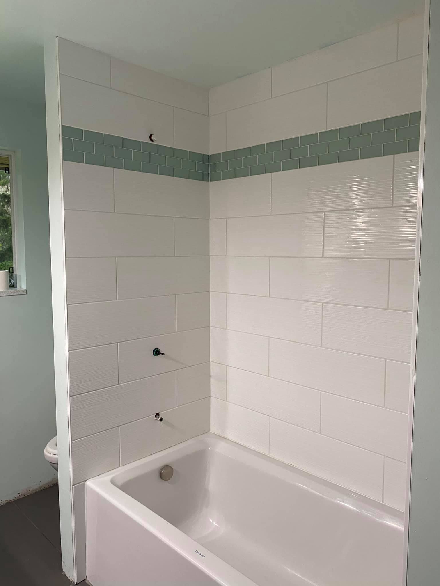 A bathtub in a bathroom with white tiles on the wall.