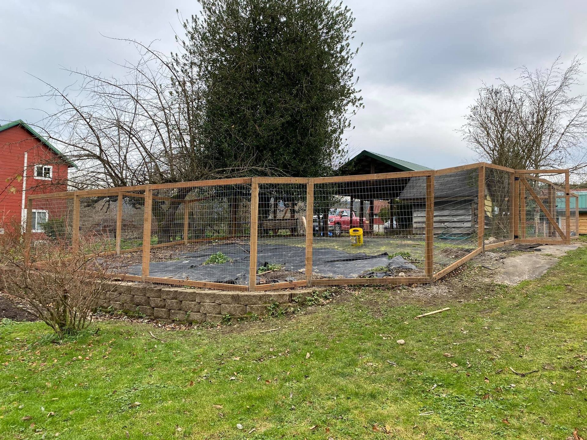 A wooden fence is surrounding a garden with a red barn in the background.