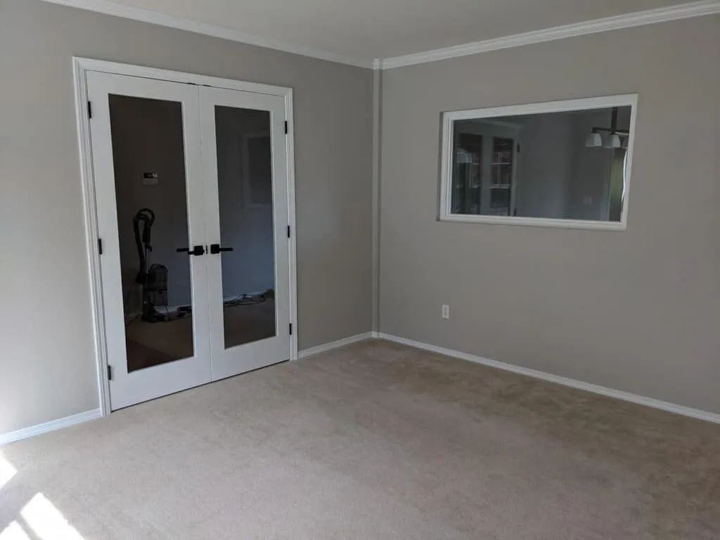 Empty room with glass-paned double doors and a framed mirror; neutral paint and light carpet.