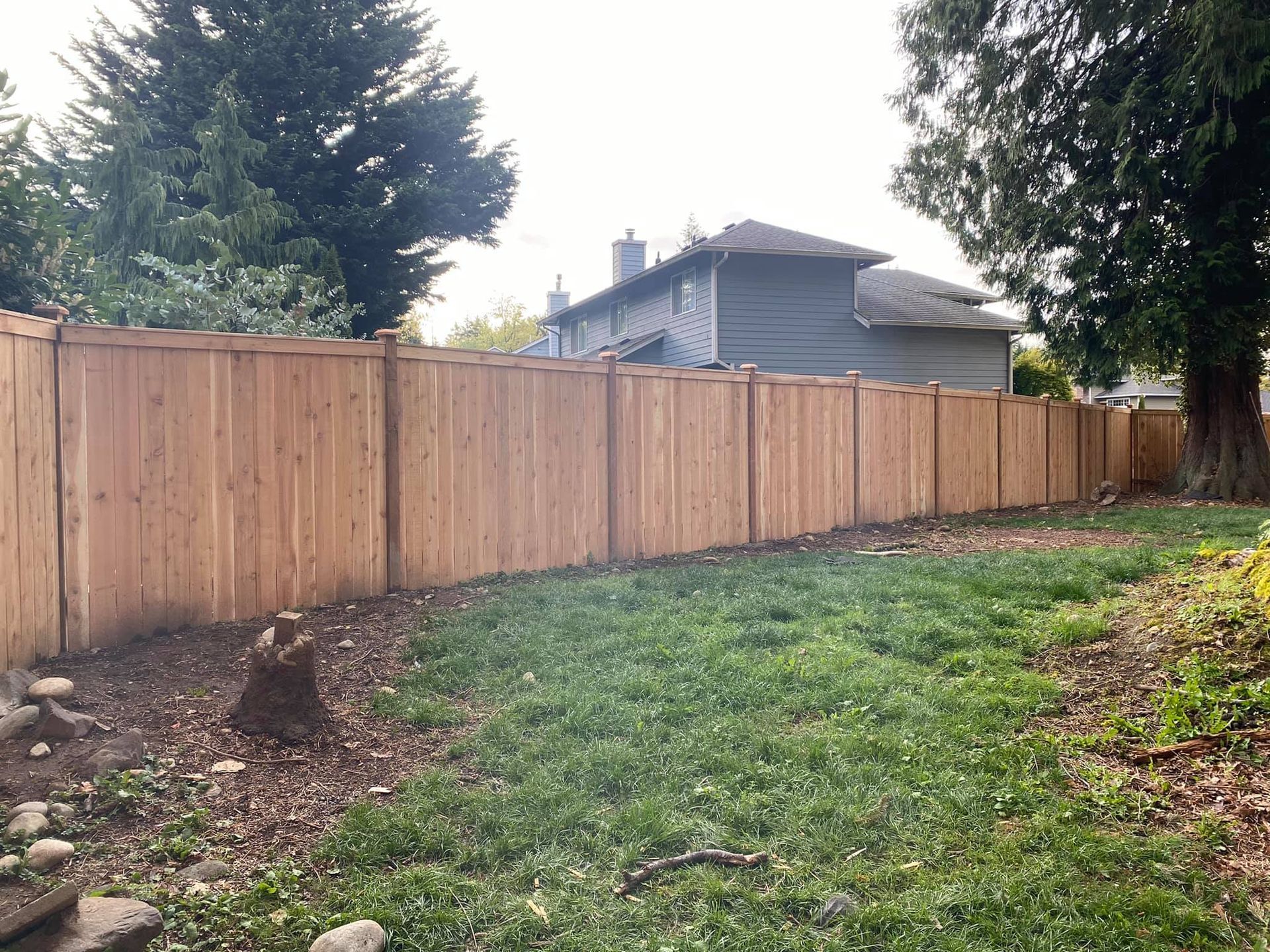 A wooden fence surrounds a lush green yard in front of a house.