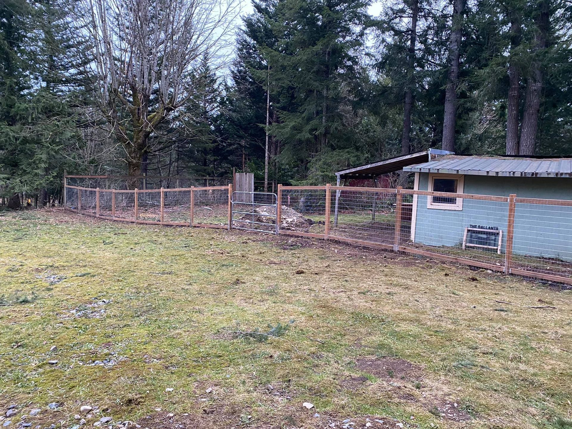 A wooden fence surrounds a grassy field with a shed in the background.