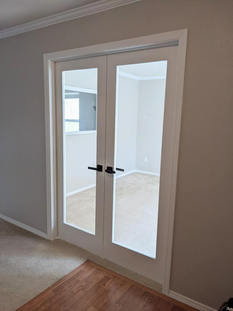A living room with a pair of french doors leading to a kitchen.