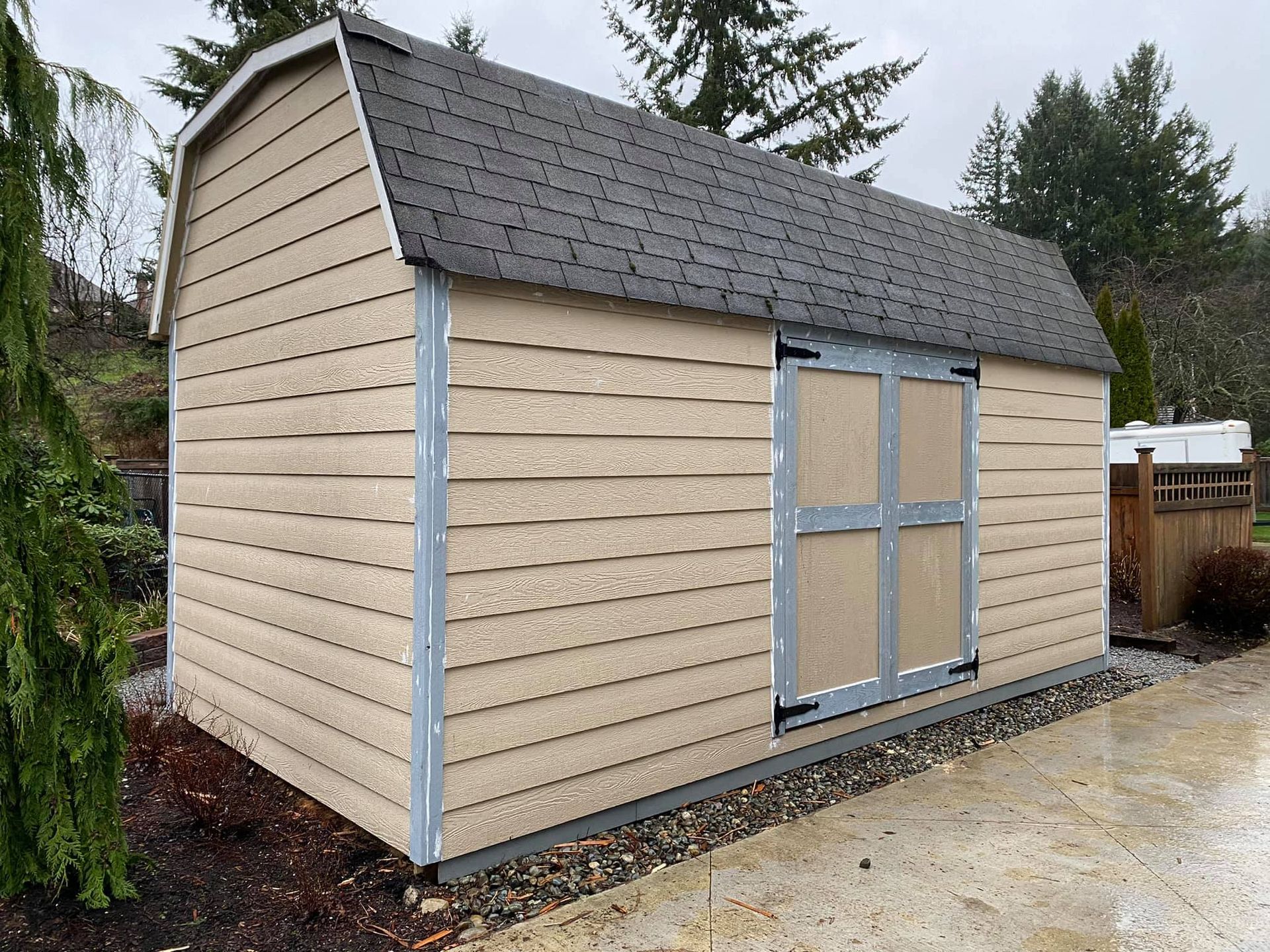 A barn shed with a black roof is sitting on top of a gravel driveway.
