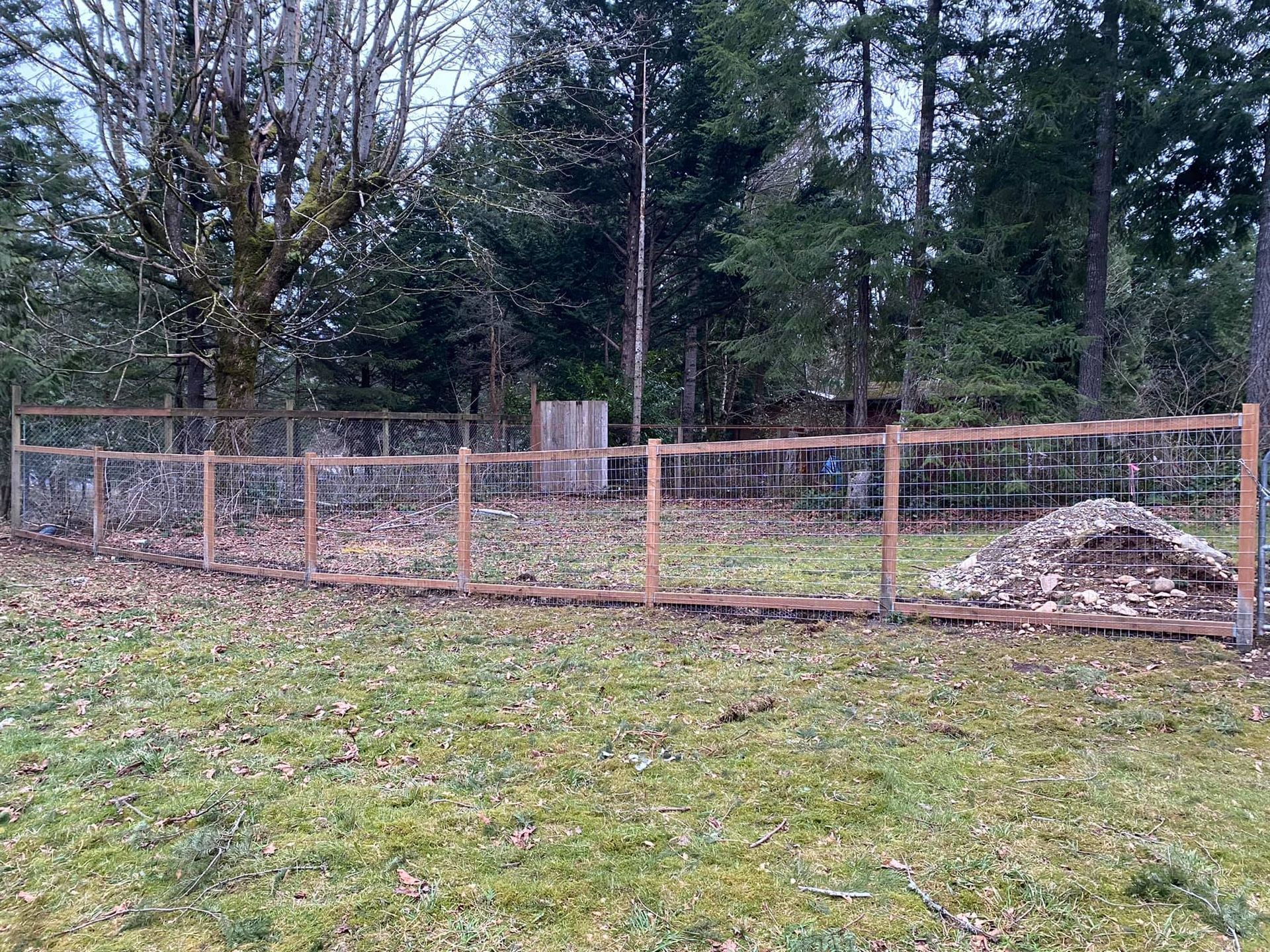 A wooden fence surrounds a grassy field with trees in the background.
