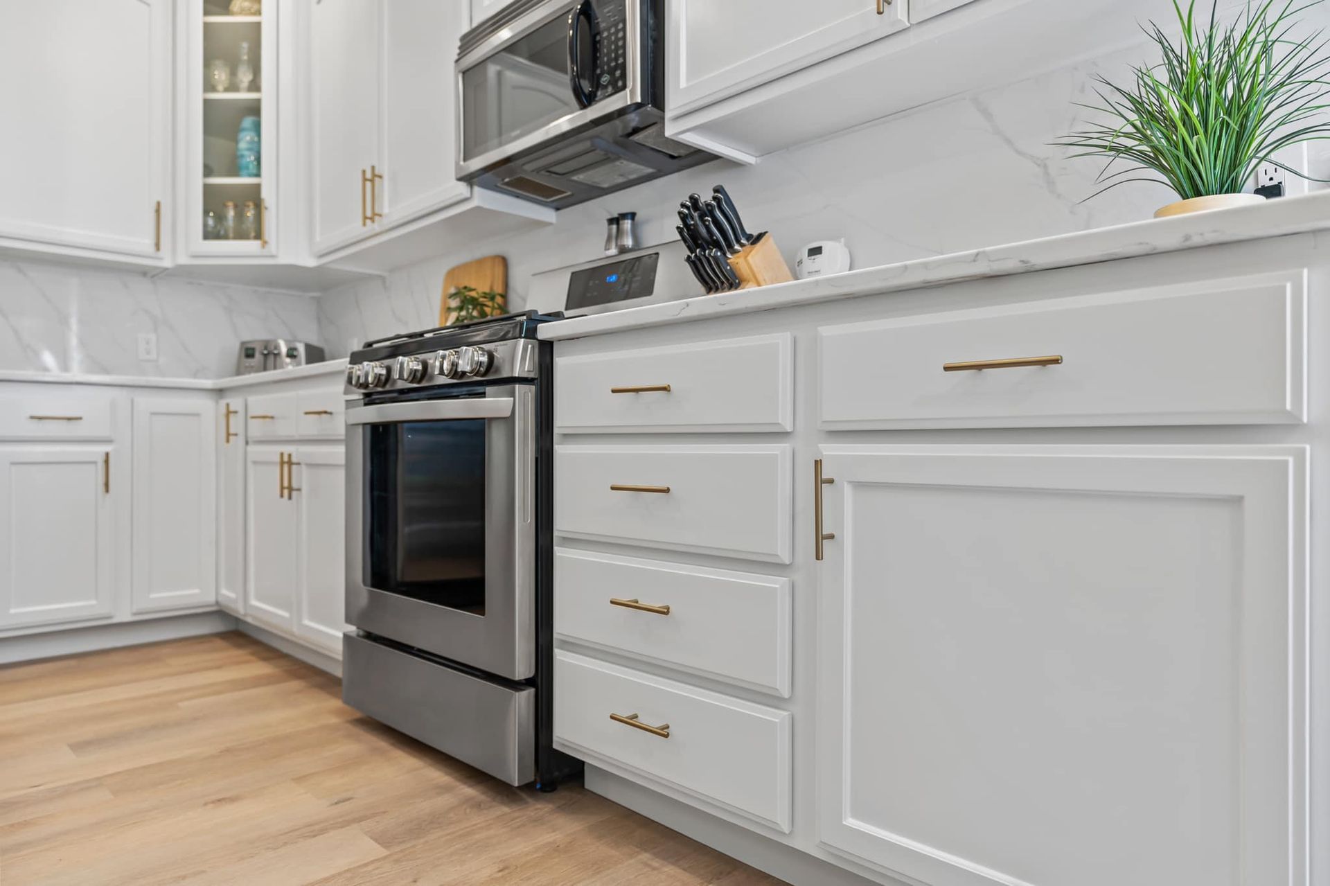 A kitchen with white cabinets , stainless steel appliances , a stove and a microwave.