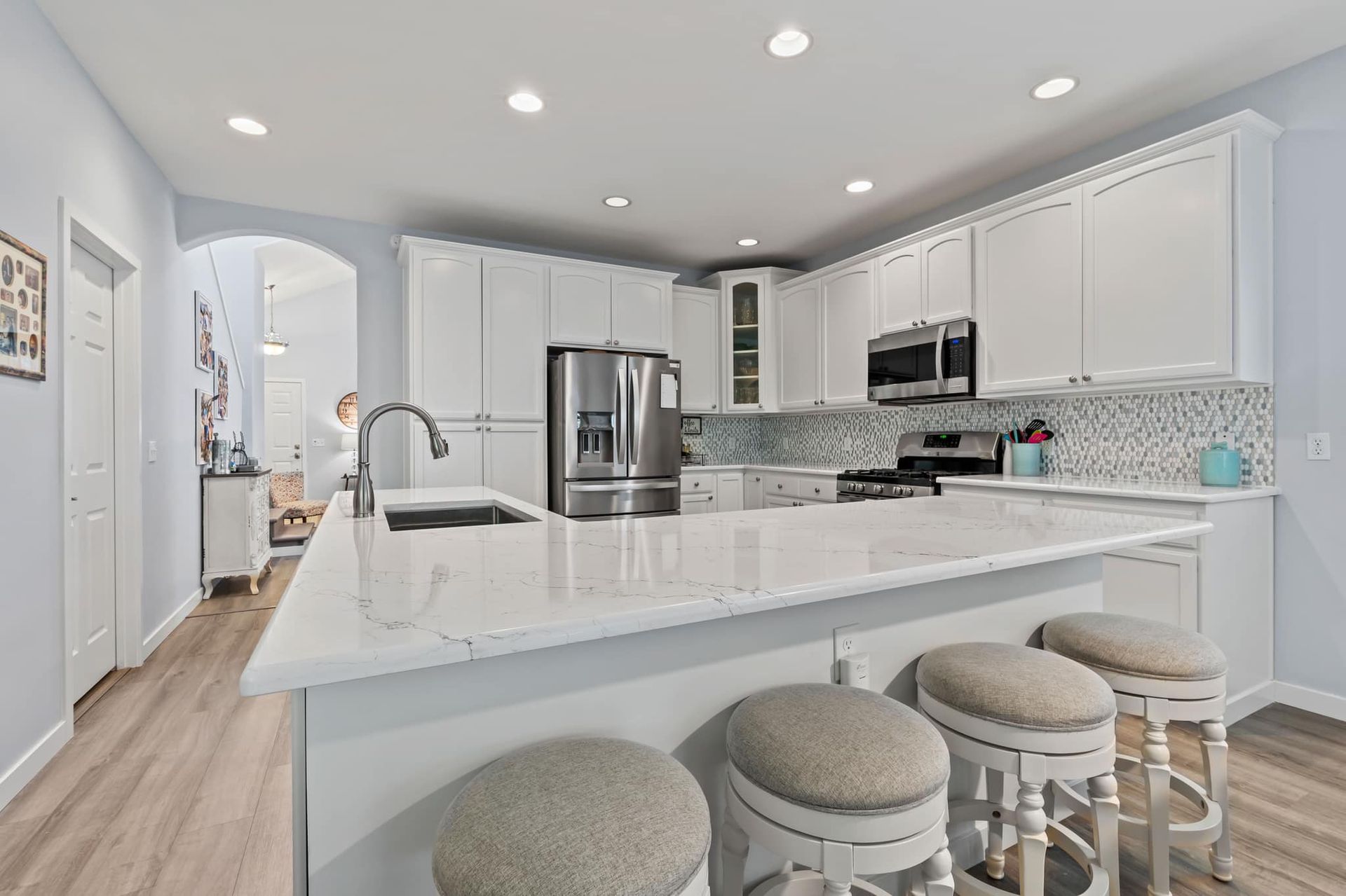 A kitchen with white cabinets and stools and a large island.