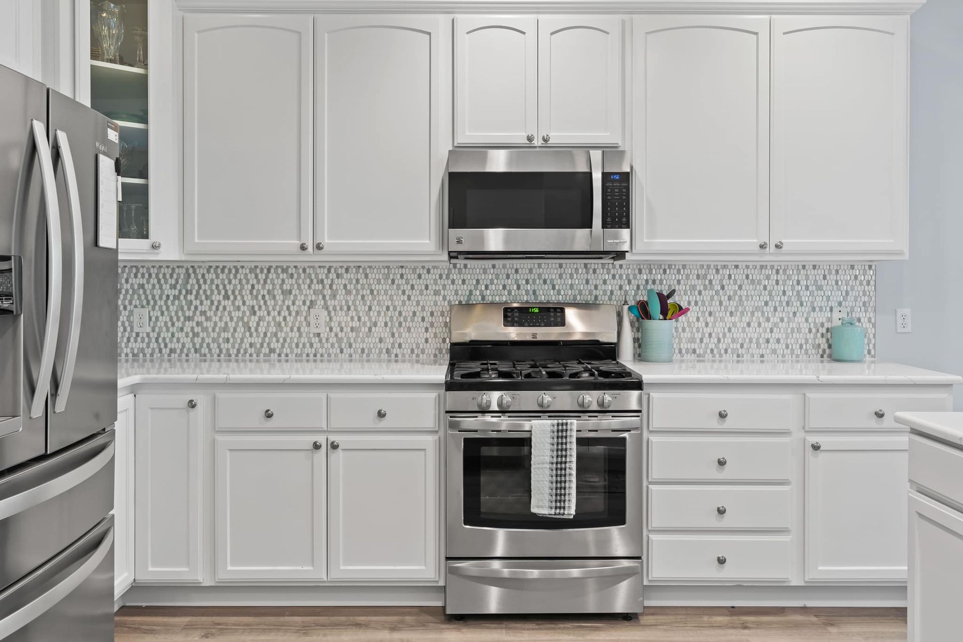 A kitchen with white cabinets , stainless steel appliances , and a refrigerator.