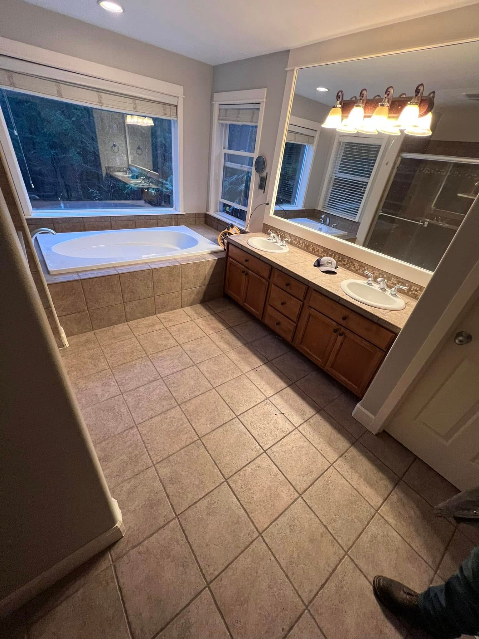 A bathroom with two sinks , a tub , and a large mirror.