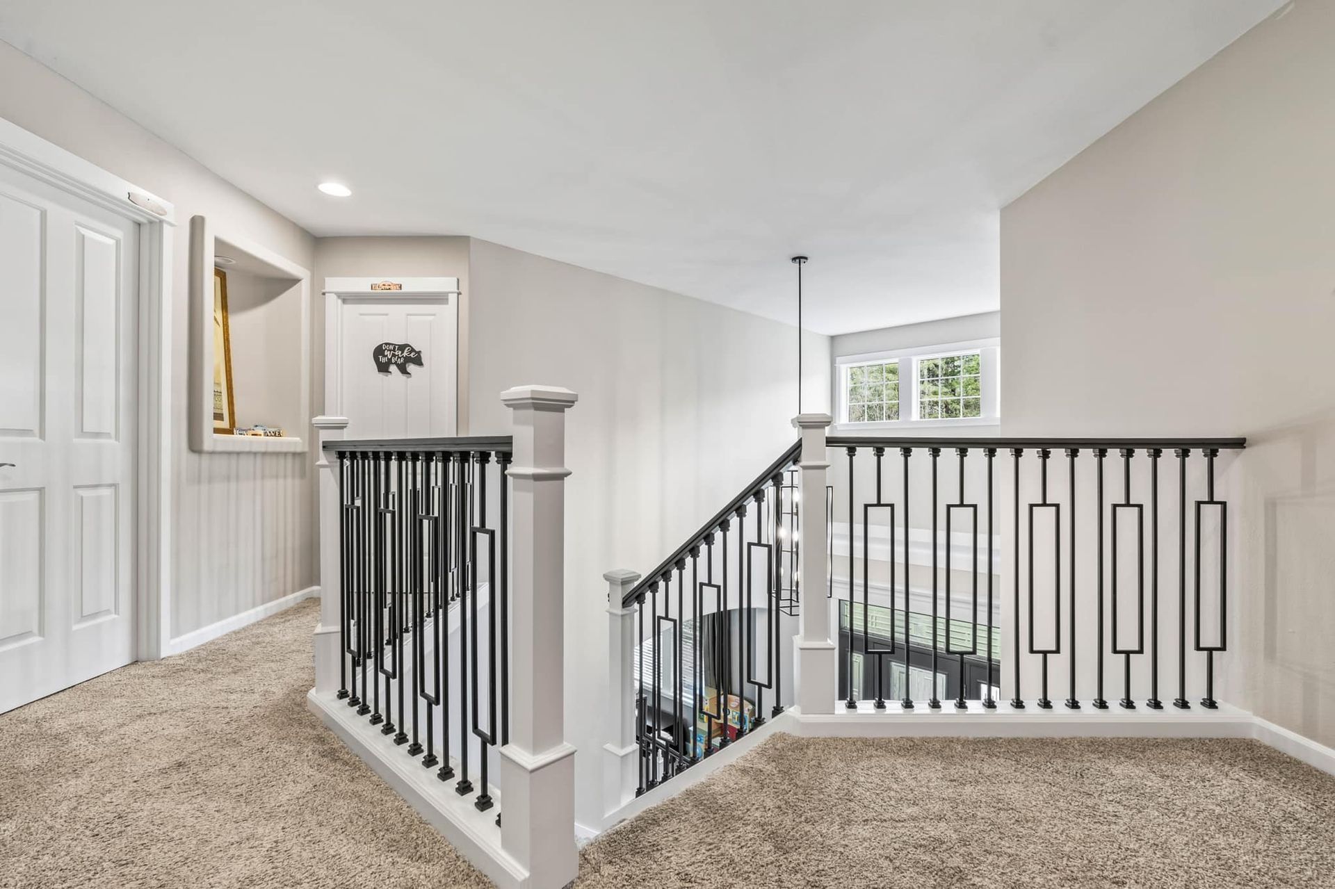 Hallway with beige carpet, white walls, and black and white railing.