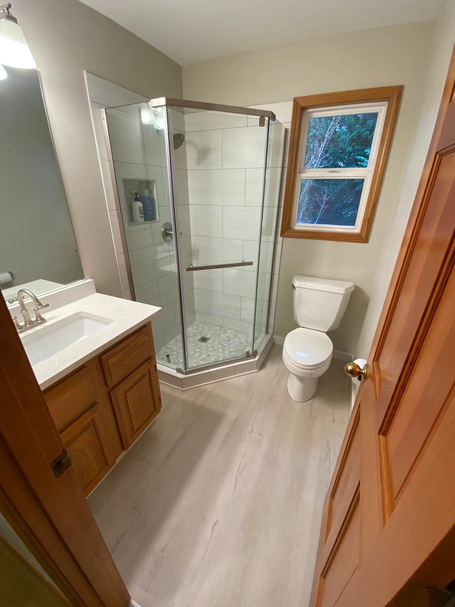 A bathroom with a toilet , sink , shower and window.