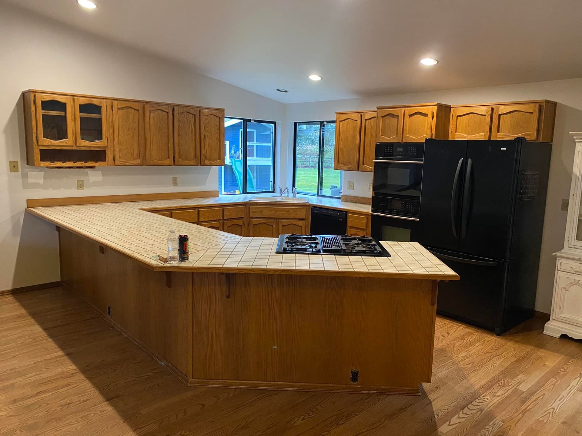 An empty kitchen with wooden cabinets and a black refrigerator.