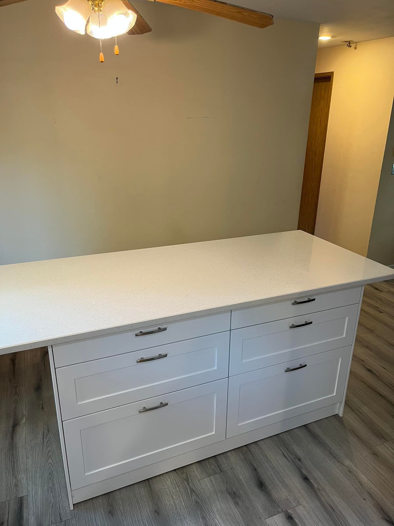 A large white island with drawers and a ceiling fan in a kitchen.
