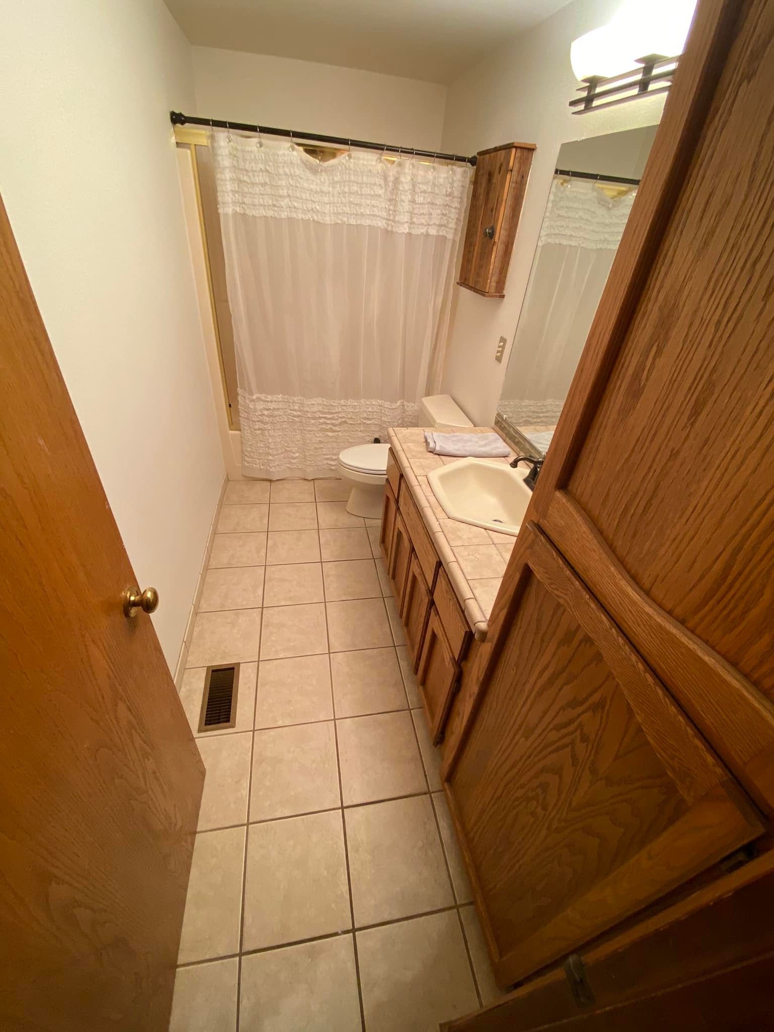 A bathroom with a toilet , sink , mirror and shower curtain.