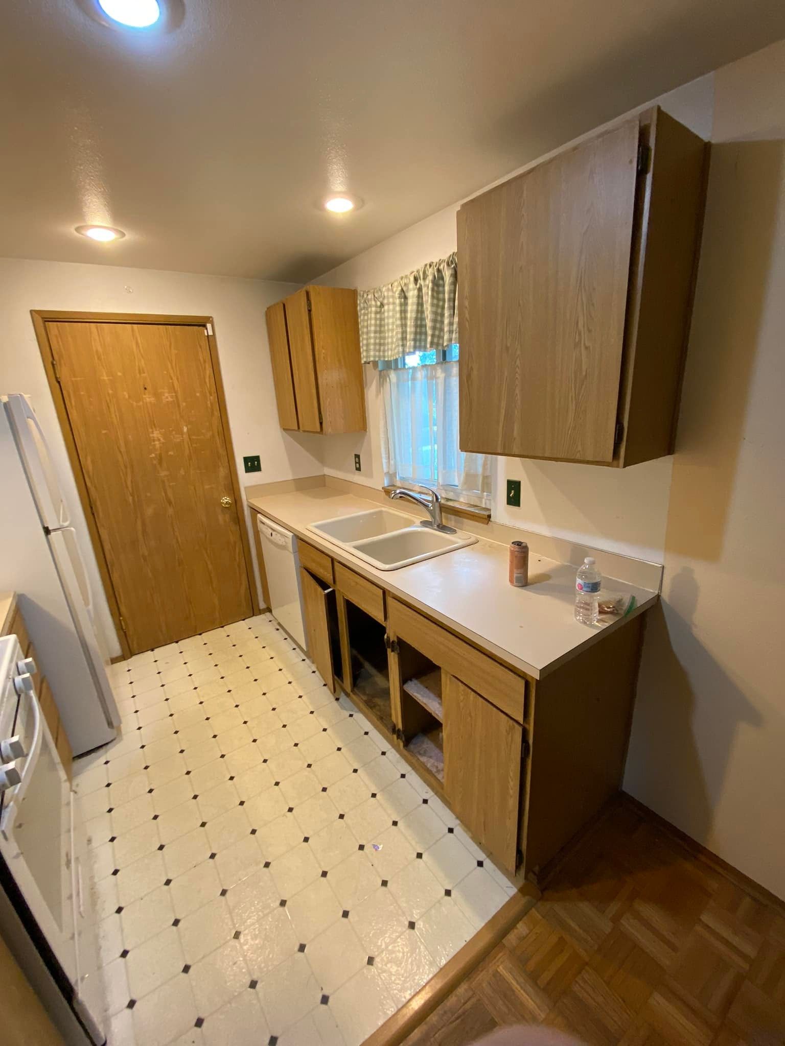 A kitchen with wooden cabinets , a sink , a refrigerator , and a window.