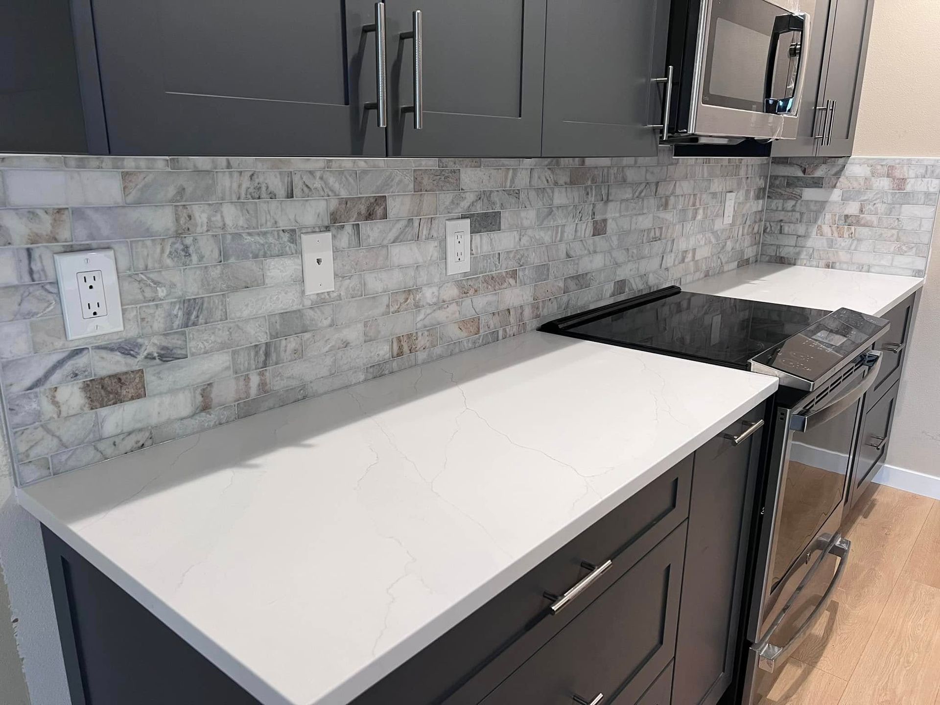 A kitchen with black cabinets , white counter tops , a stove and a microwave.
