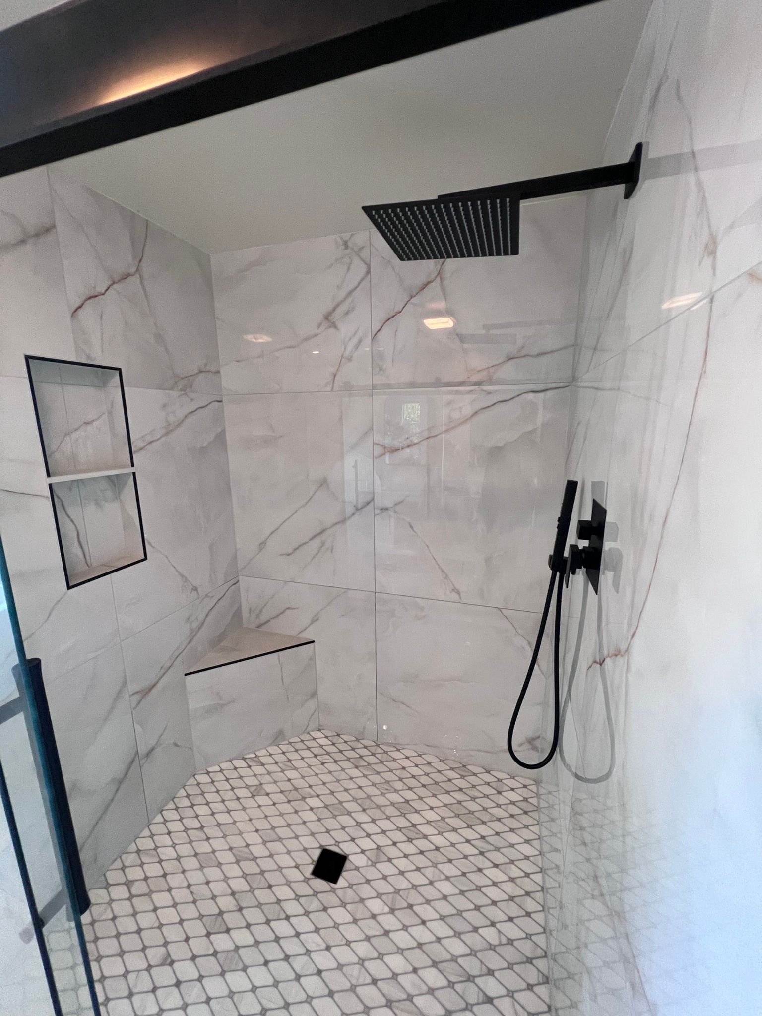 A bathroom with white tiles and a black shower head.