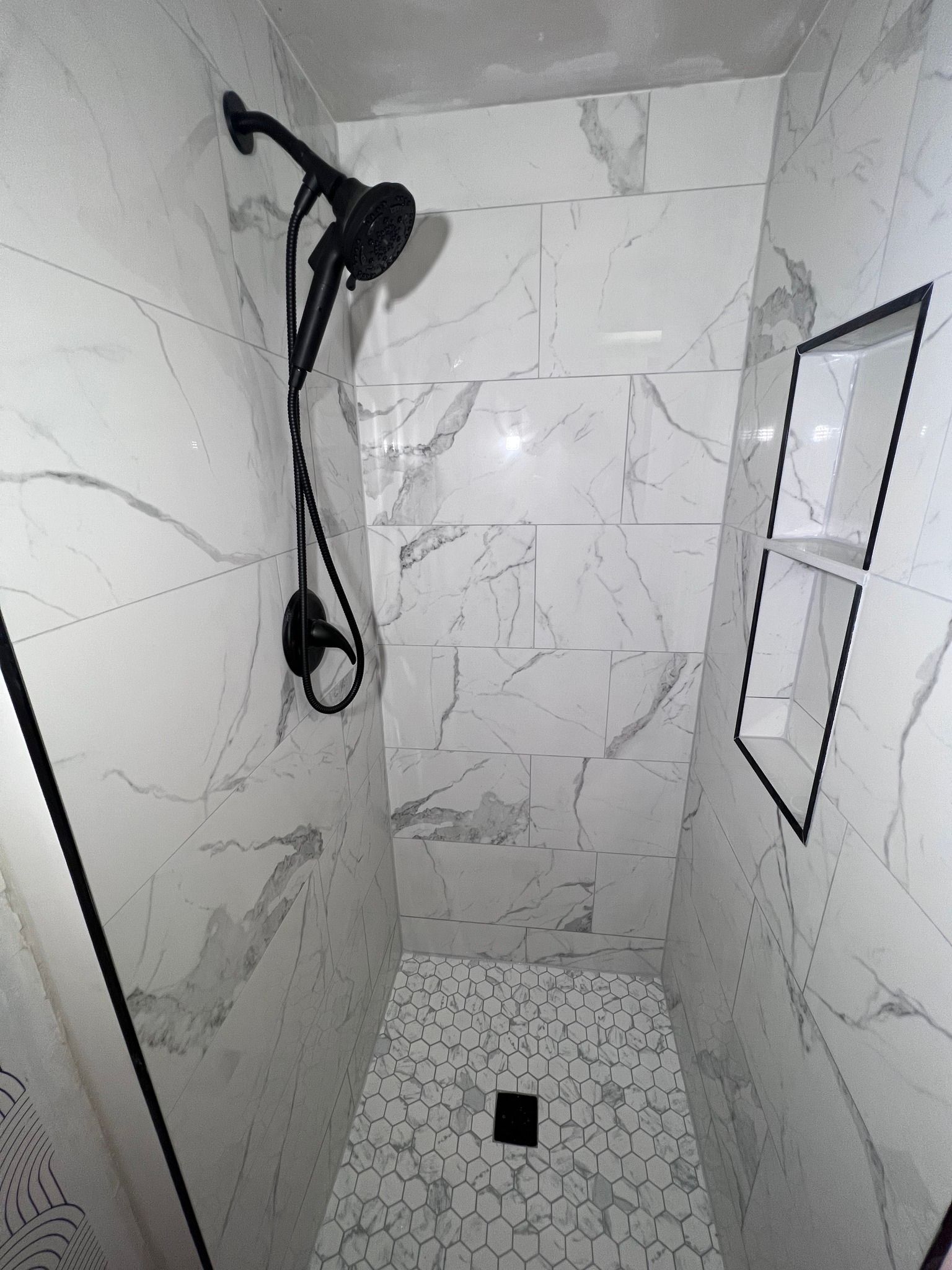 A shower with marble tiles and a black shower head.