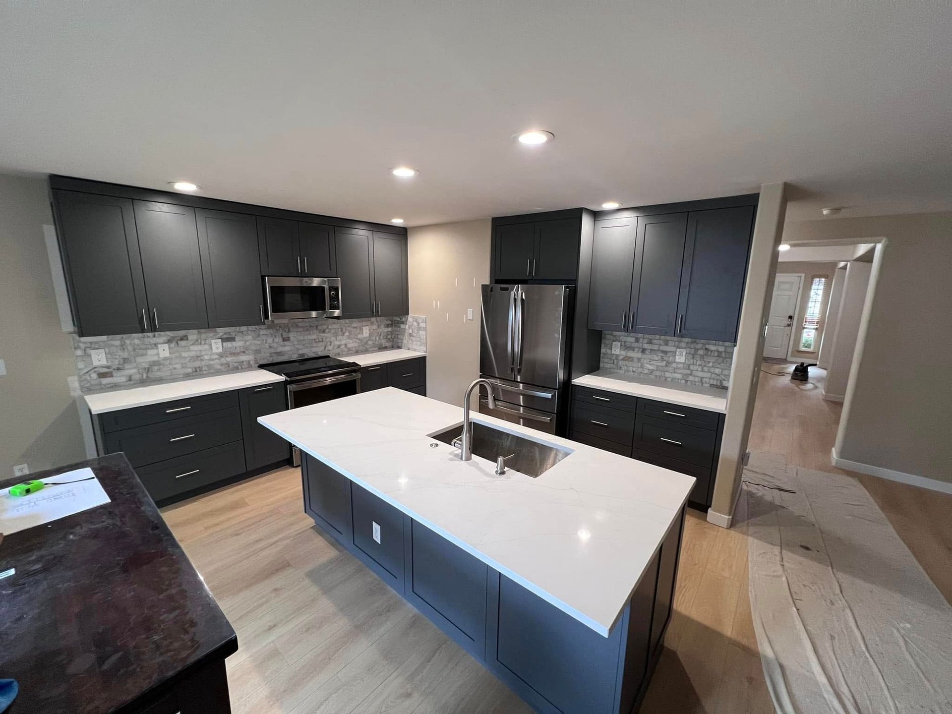 A kitchen with black cabinets , white counter tops , stainless steel appliances and a large island.