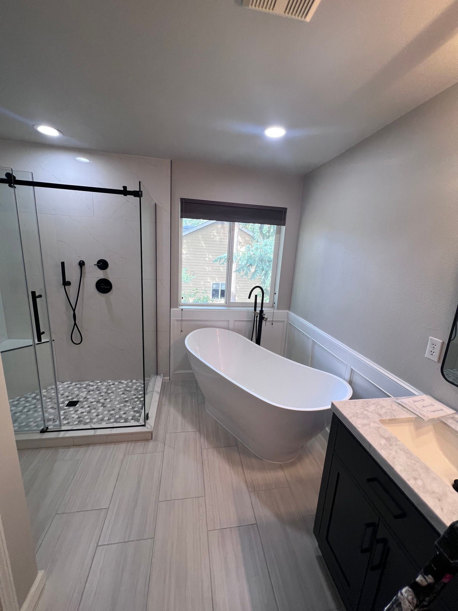 A bathroom with a bathtub , sink , shower and window.