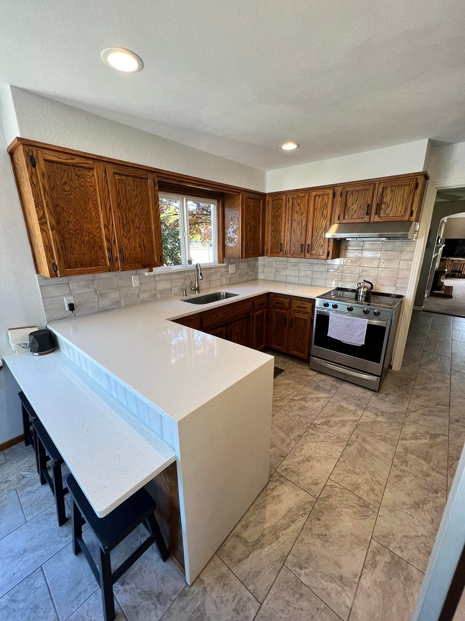A kitchen with wooden cabinets , white counter tops , a stove and a sink.