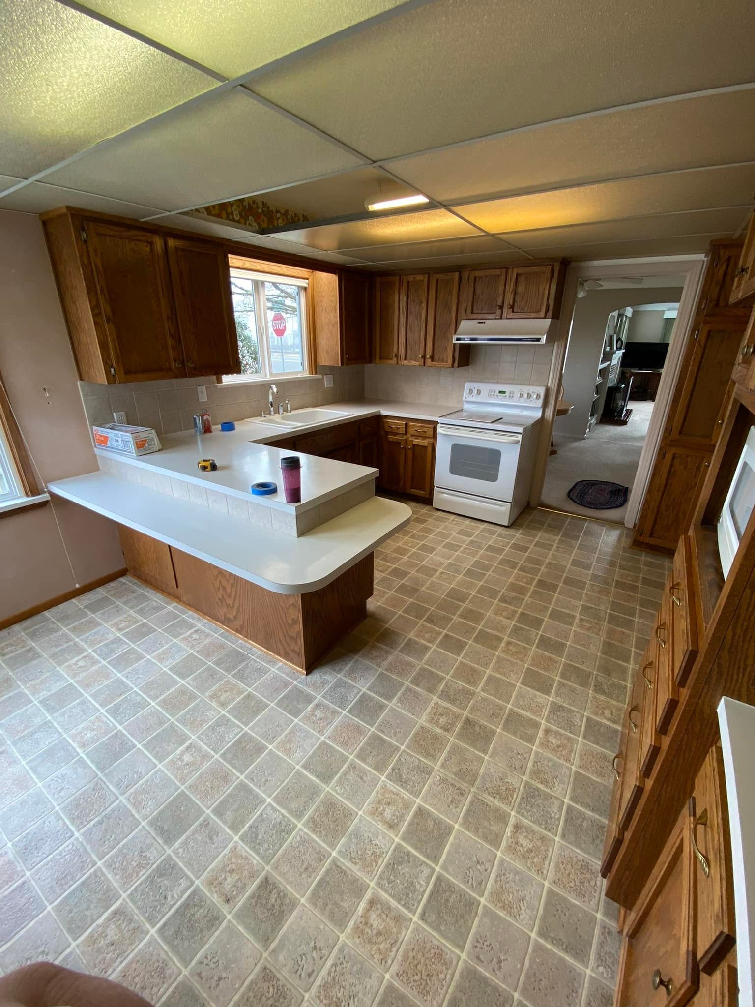 A kitchen with a stove , sink , cabinets and tile floor.