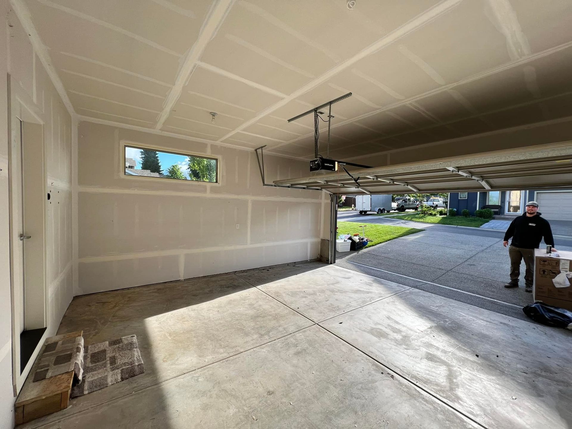 A man is standing in a garage with a garage door open.