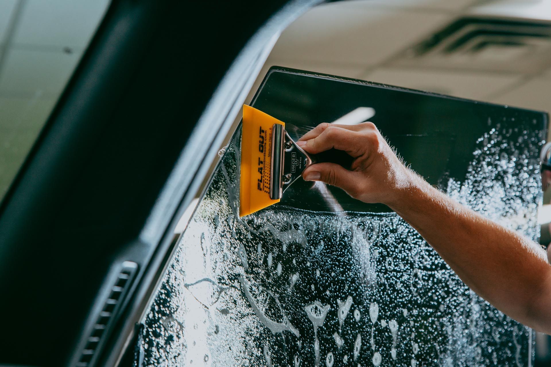 Person using a squeegee to apply tinted film to a car window.