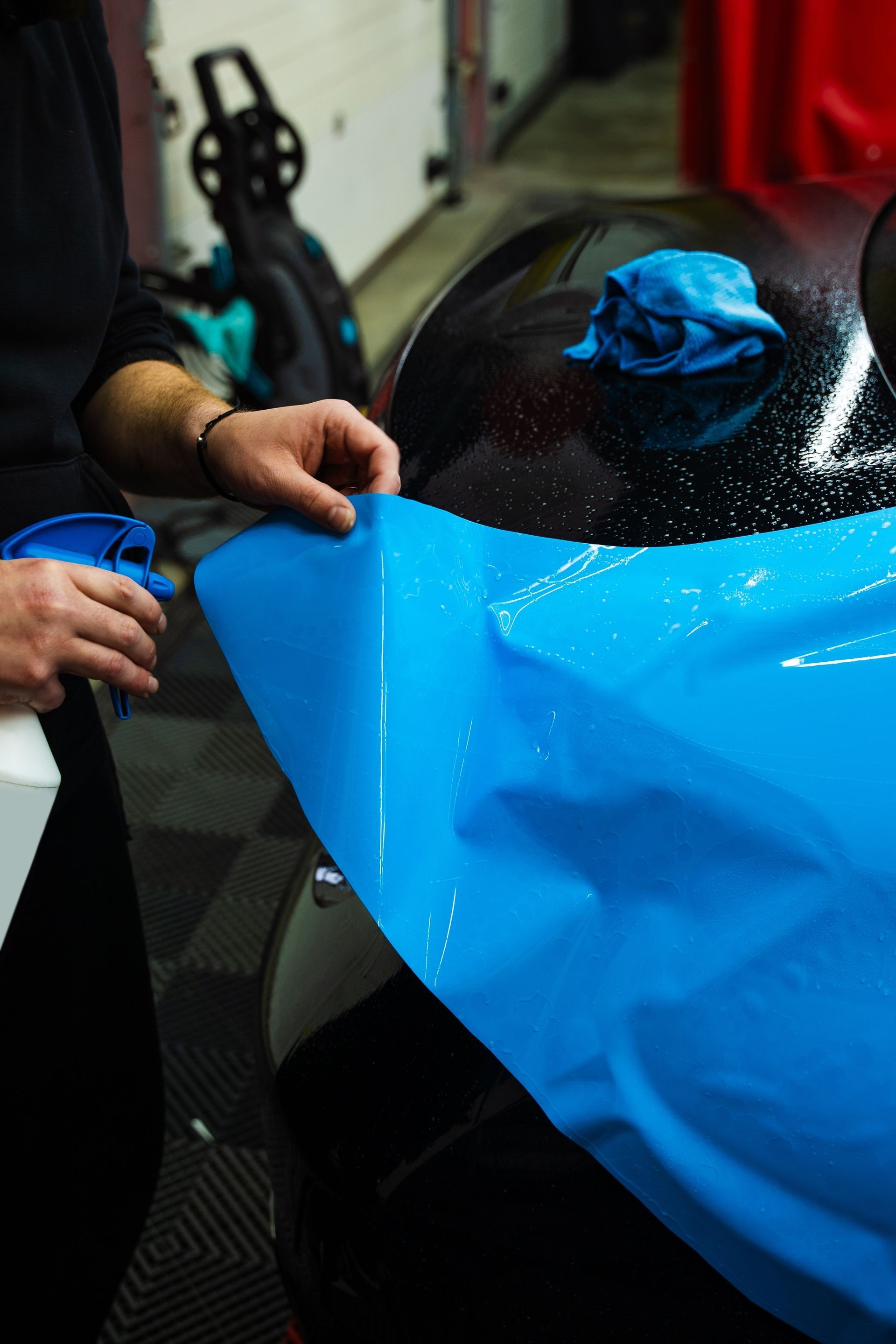Person spraying blue film onto a black car window.