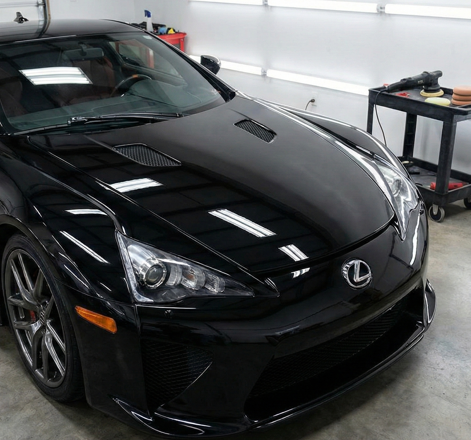 Black Lexus LFA sports car in a brightly lit garage, reflecting the overhead lights.