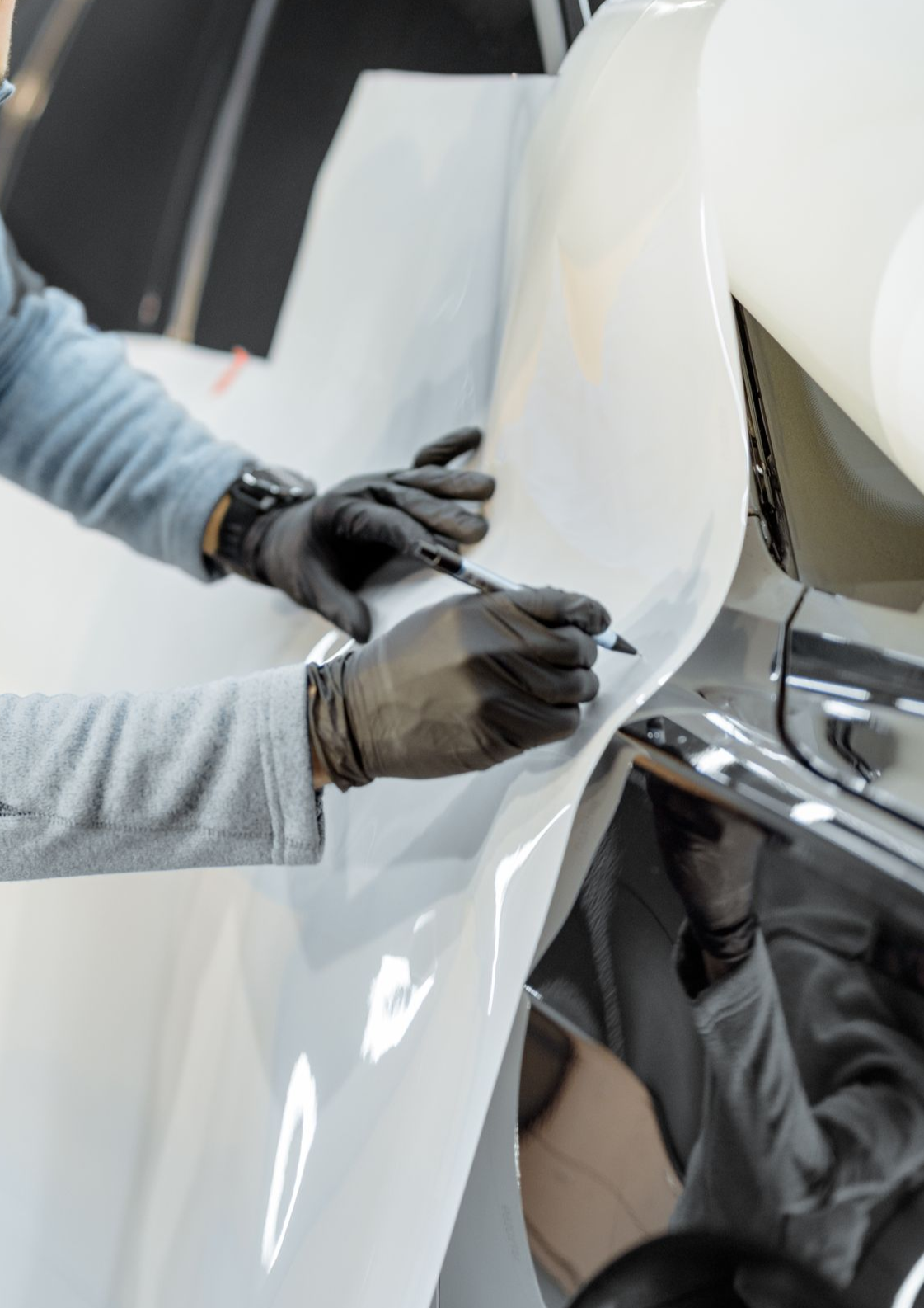 Person wearing black gloves marking white vinyl on a car with a pen.