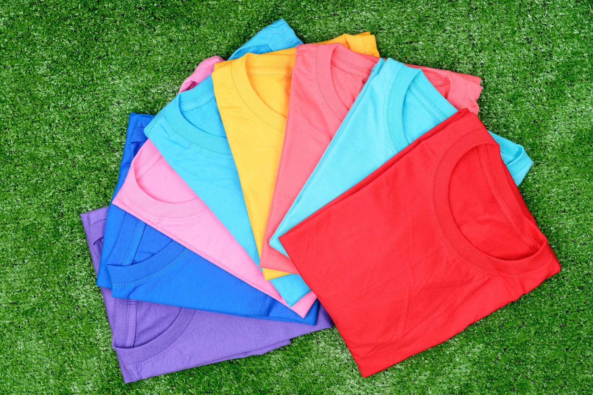 Stack of colorful t-shirts on green grass.
