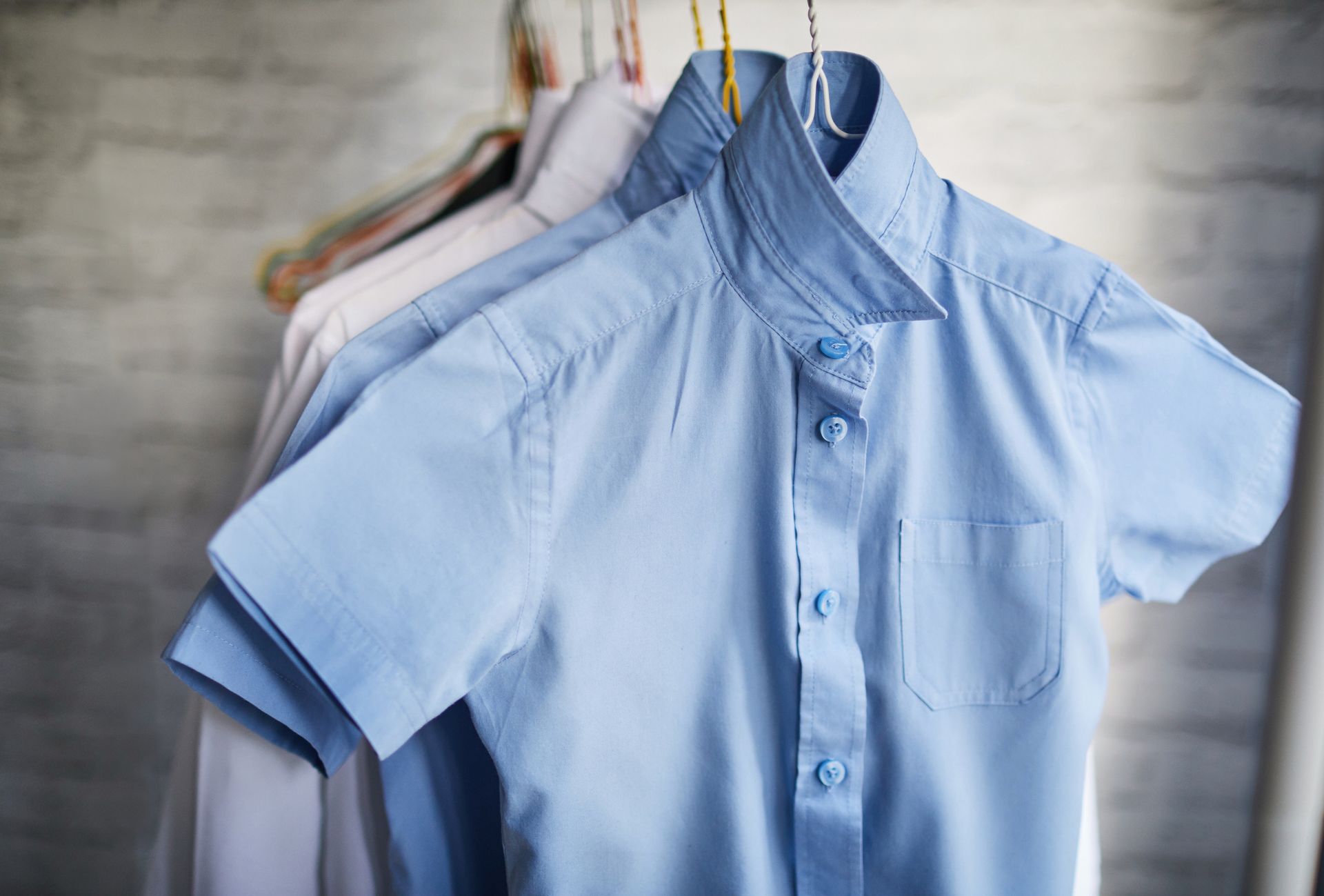 Light blue short-sleeved collared shirt on a hanger with other shirts in the background.