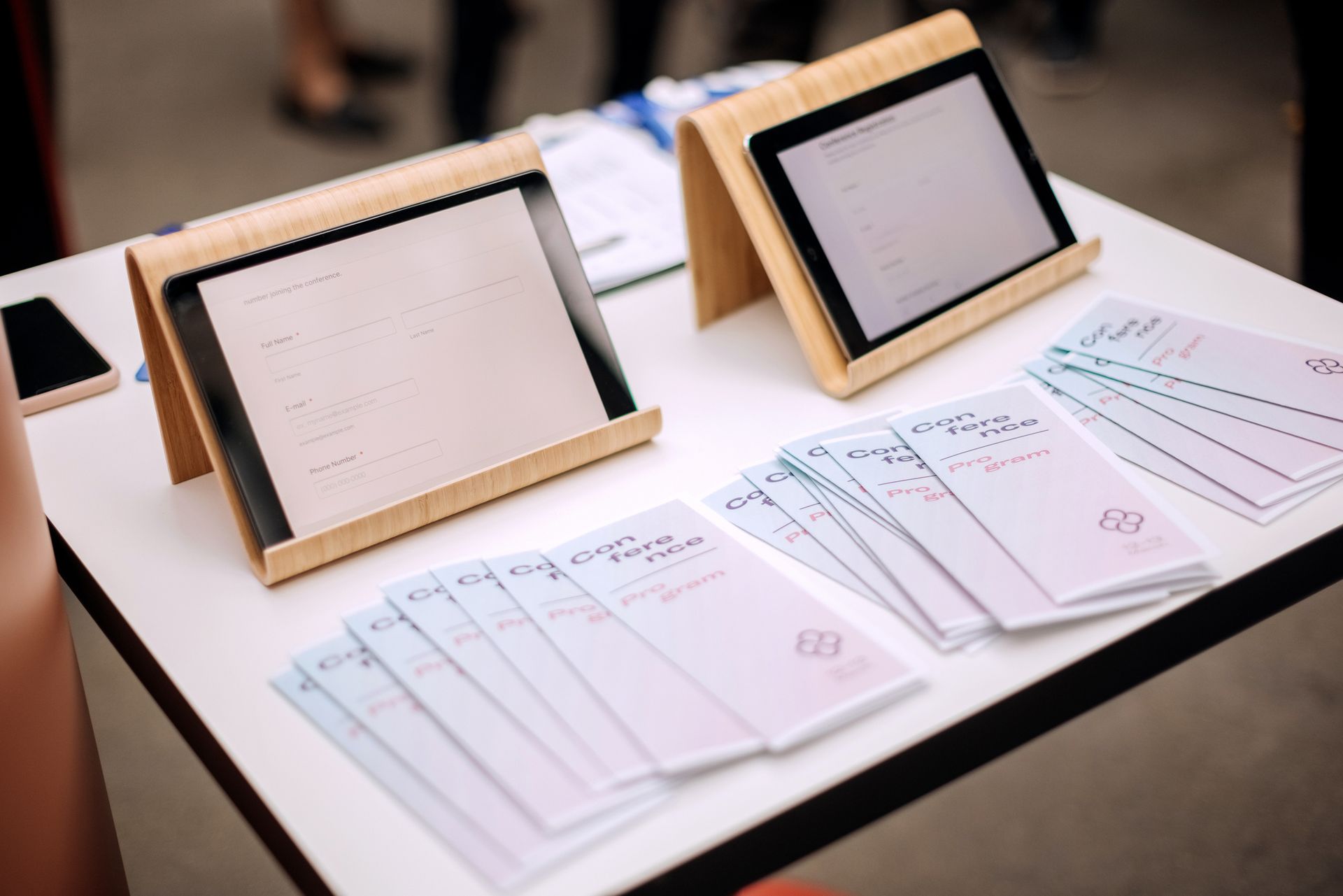 Table with two tablets in wooden stands, stacked papers, and a phone.