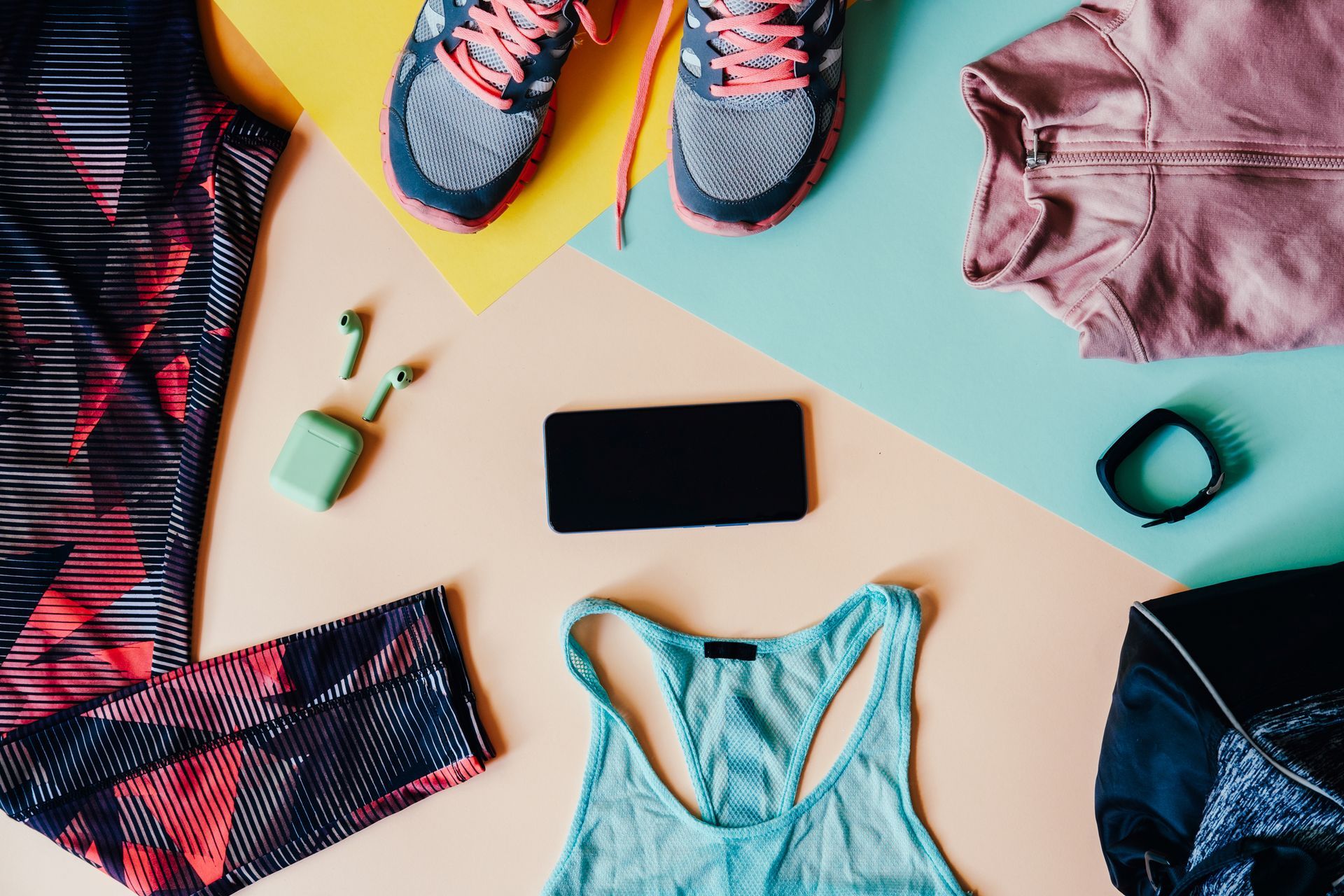 Fitness gear arranged on a colorful background, including sneakers, leggings, shirt, fitness tracker, phone, and headphones.