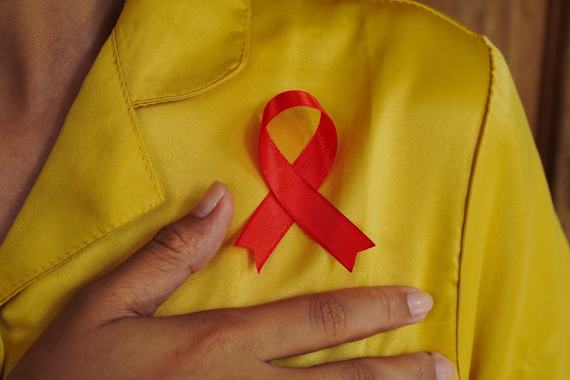 Red ribbon pinned on yellow shirt, hand on chest.